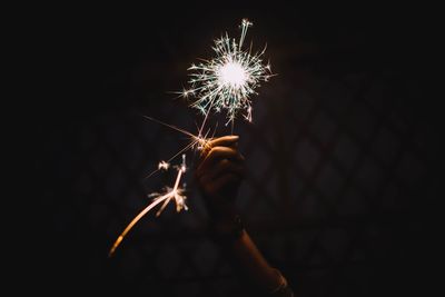 Cropped hand of woman holding lit sparkler at night