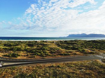 Road amidst field by sea against sky