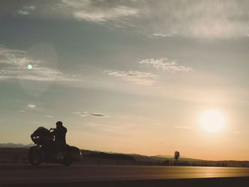 Silhouette man riding motorcycle on road against sky during sunset