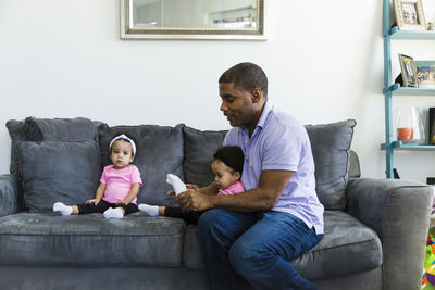 Father putting socks on daughter's foot while sitting on sofa