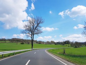 Road by trees on field against sky