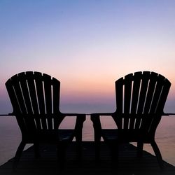 Silhouette chairs on beach against clear sky during sunset