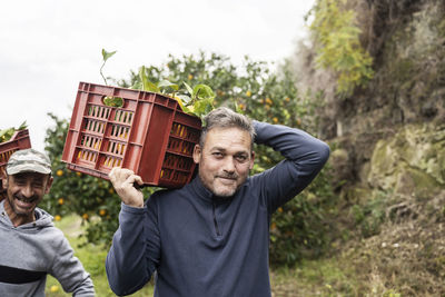 Smiling man carrying red crates of fresh oranges in farm