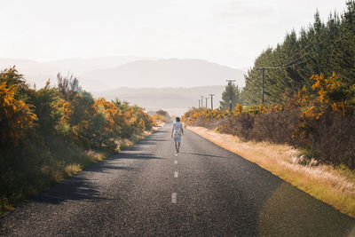 New zealand, north island, rotorua, rear view of young man walking on road in bay of plenty