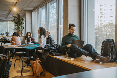 Young man using laptop sitting near friends in community college cafeteria