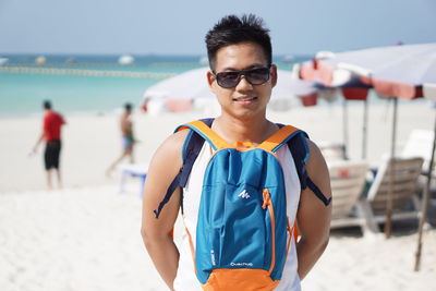 Portrait of man wearing bag while standing at beach against sky