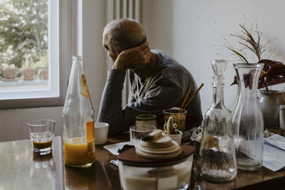 Senior man with hand behind head looking through window in living room