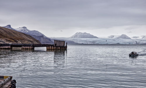 Scenic view of the arctic ocean in front of a glacier with snow capped mountains against sky