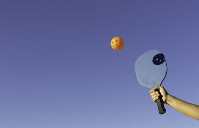 Cropped hand holding balloon against clear sky