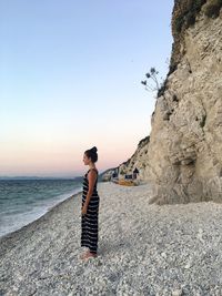 Man standing on rock at beach against clear sky