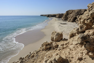 Cliff and wild beach at the coast of ras al jinz with calm water and blue skies, sultanate of oman.