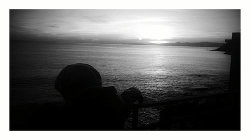 Rear view of silhouette man sitting on sea against sky