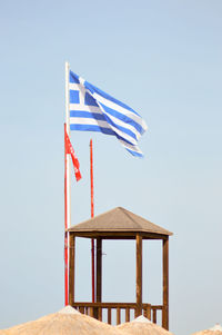 Greek flag by lookout tower at beach against clear sky