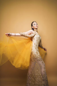 Portrait of young woman standing against yellow background