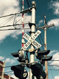 Low angle view of railroad crossing sign against sky