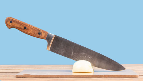 Kitchen knife in an onion half on a cutting board against a blue background. copy space.