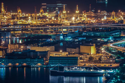 Illuminated factory by river against sky at night