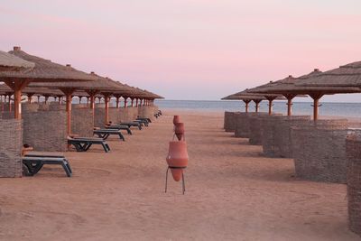 Deck chairs on beach against sky during sunset