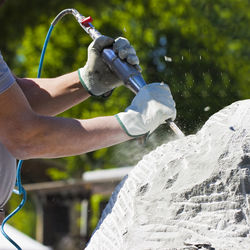 Close-up of man making sculpture with tool against trees