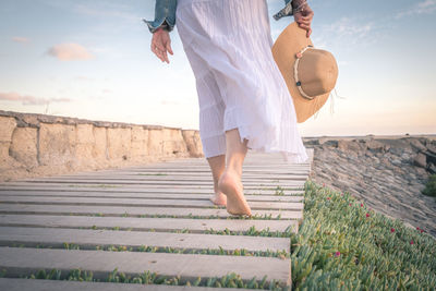 Low section of woman walking on boardwalk against sky