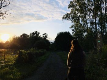 Rear view of woman standing by trees against sky during sunset