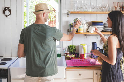 Man and woman arranging cups on shelf in kitchen at home