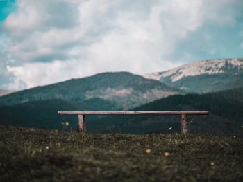 Empty bench on land against sky