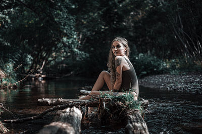 Portrait of young woman sitting on rock in lake