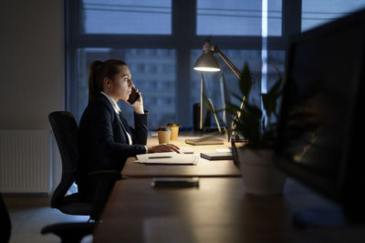 Businesswoman talking on phone while working at office at night