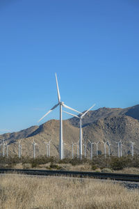 Windmills on field against clear blue sky