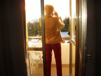 Full length of woman using phone while standing on window