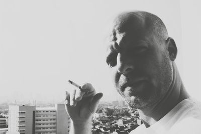 Close-up portrait of man smoking cigarette against city on sunny day