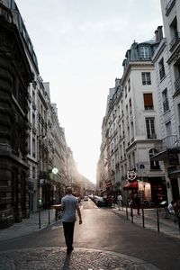 Rear view of man walking on road along buildings