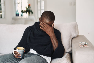 Tired man holding coffee cup while sitting on sofa