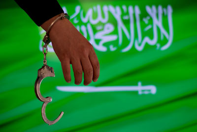 Cropped hand of male criminal with handcuffs against saudi arabian flag