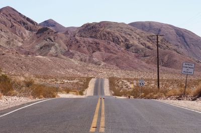 Road leading towards mountains against clear sky
