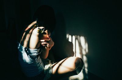 Woman hugging self while sitting against wall at home