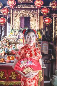 Portrait of teenager holding hand fan standing at temple