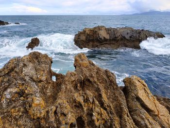 Rocks on shore by stormy ocean against sky