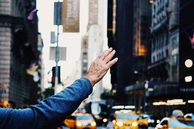 Cropped hand of man hailing taxi in city