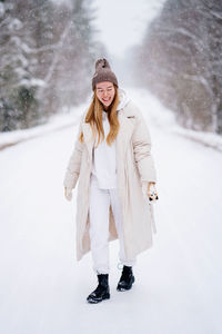 Caucasian woman in white warm jacket walking in winter forest. winter clothing. enjoying snow