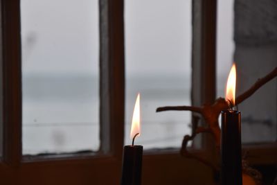 Close-up of lit candle against window
