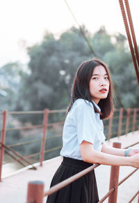 Portrait of young woman standing against railing