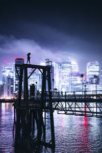 Silhouette bridge over river against sky in city