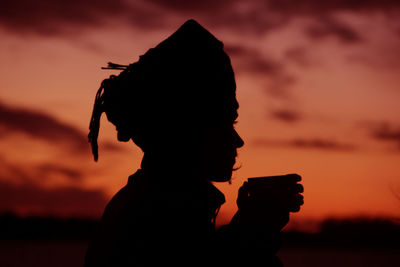 Portrait of silhouette man holding orange against sky during sunset