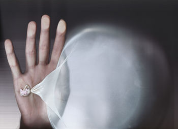 Cropped image of hand with balloon seen through glass