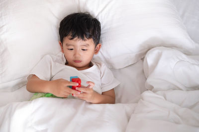 High angle view of cute boy playing with toy while lying on bed at home