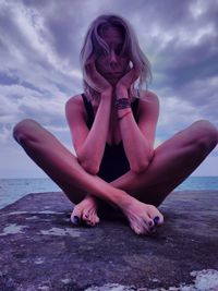 Young woman sitting on beach against sky