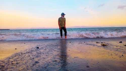 Rear view of man standing on beach against sky during sunset