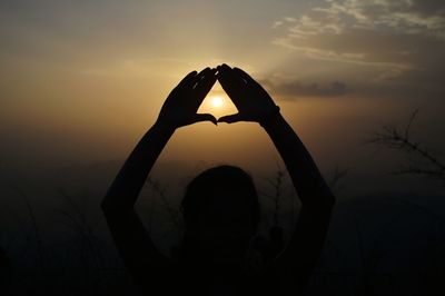 Silhouette woman making heart shape against sky during sunset